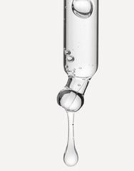 Pipeta con sérum transparente liberando una gota sobre fondo neutro.