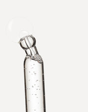 Pipeta con sérum transparente liberando una gota sobre fondo neutro.
