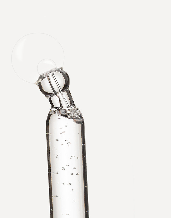 Pipeta con sérum transparente liberando una gota sobre fondo neutro.