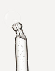 Pipeta con sérum transparente liberando una gota sobre fondo neutro.